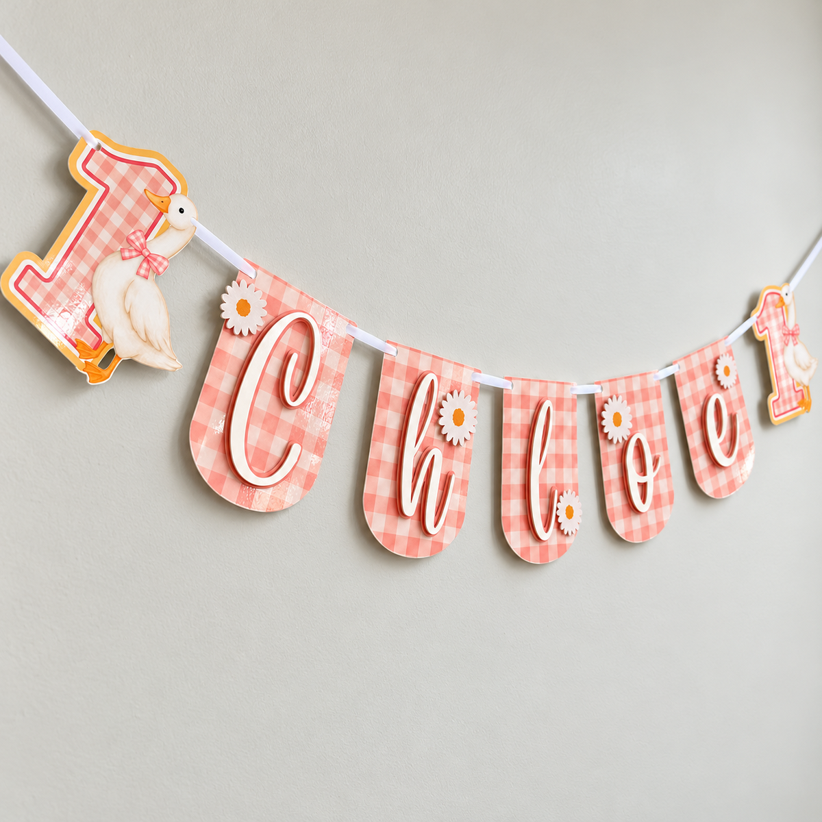 Angled view of the pink gingham One Silly Goose birthday banner personalized with Chloe, showing layered lettering and daisy accents.