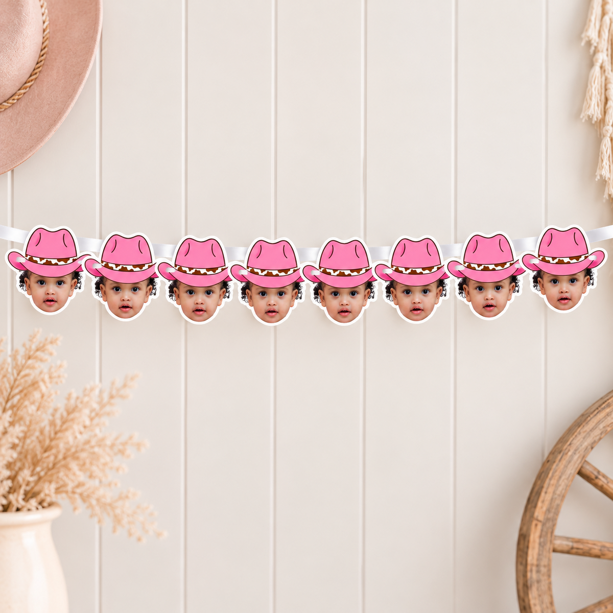 Personalized pink cowgirl hat photo banner displayed above a My First Rodeo dessert table with pink balloons cow print accents cake cupcakes boots rope and western party decor