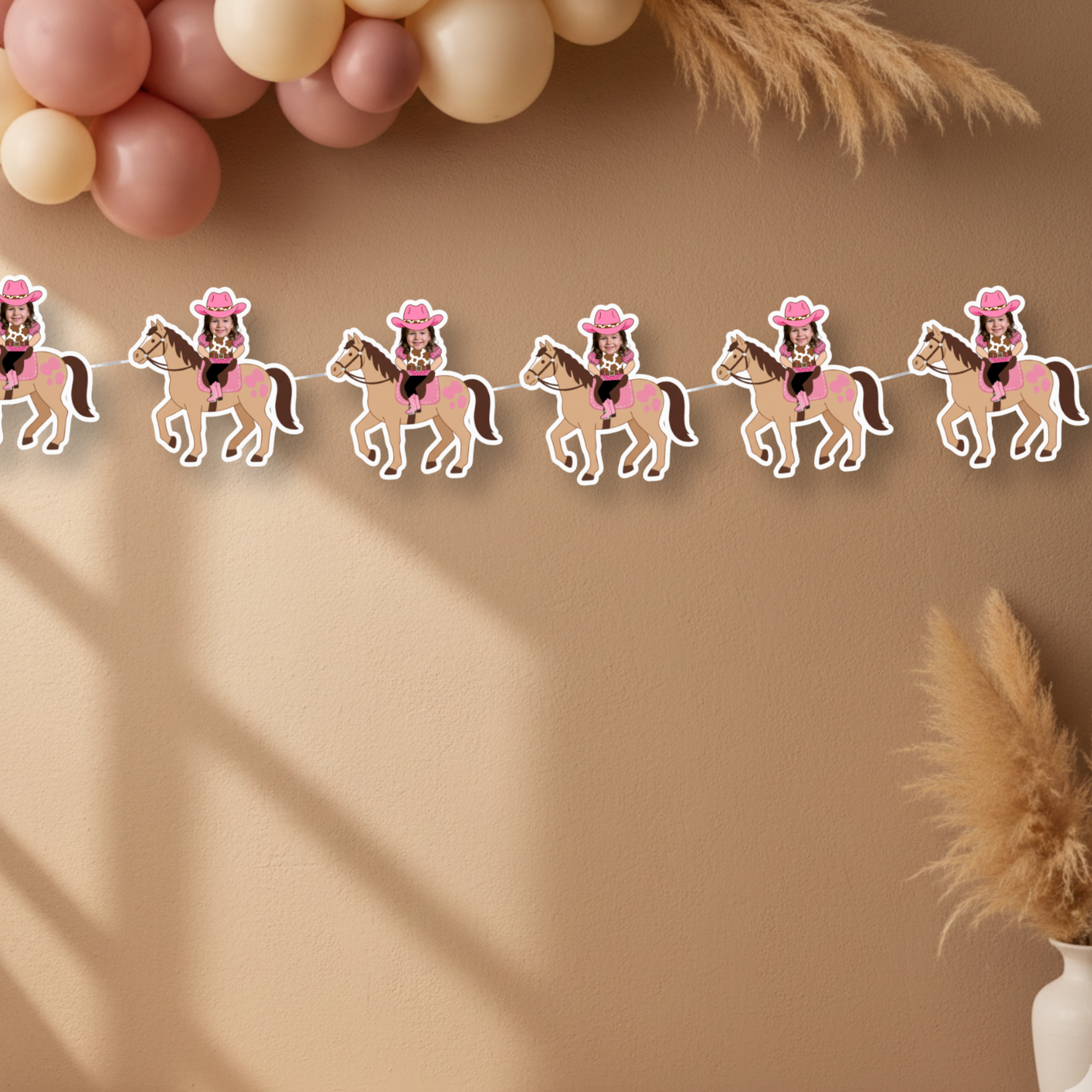 Pink rodeo birthday banner with custom cowgirl photo panels displayed on a warm desert-inspired wall with neutral balloons and pampas grass. This soft western themed party backdrop showcases the personalized cowgirl banner for smash cake photos, pink rodeo birthdays, and boho cowgirl celebrations.