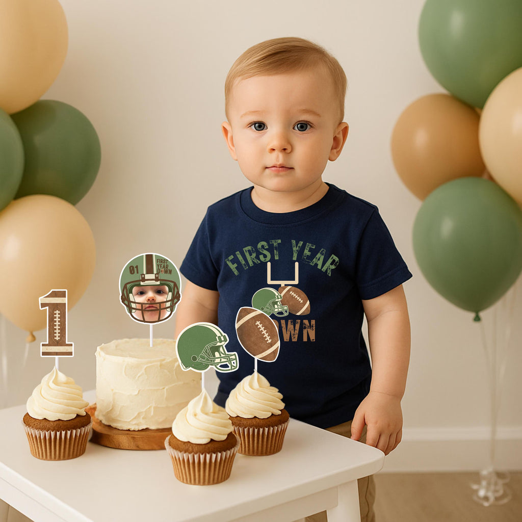 A young boy standing by a smash cake decorated with custom football helmet and '1' yard line cupcake toppers for a Rookie of the Year theme.