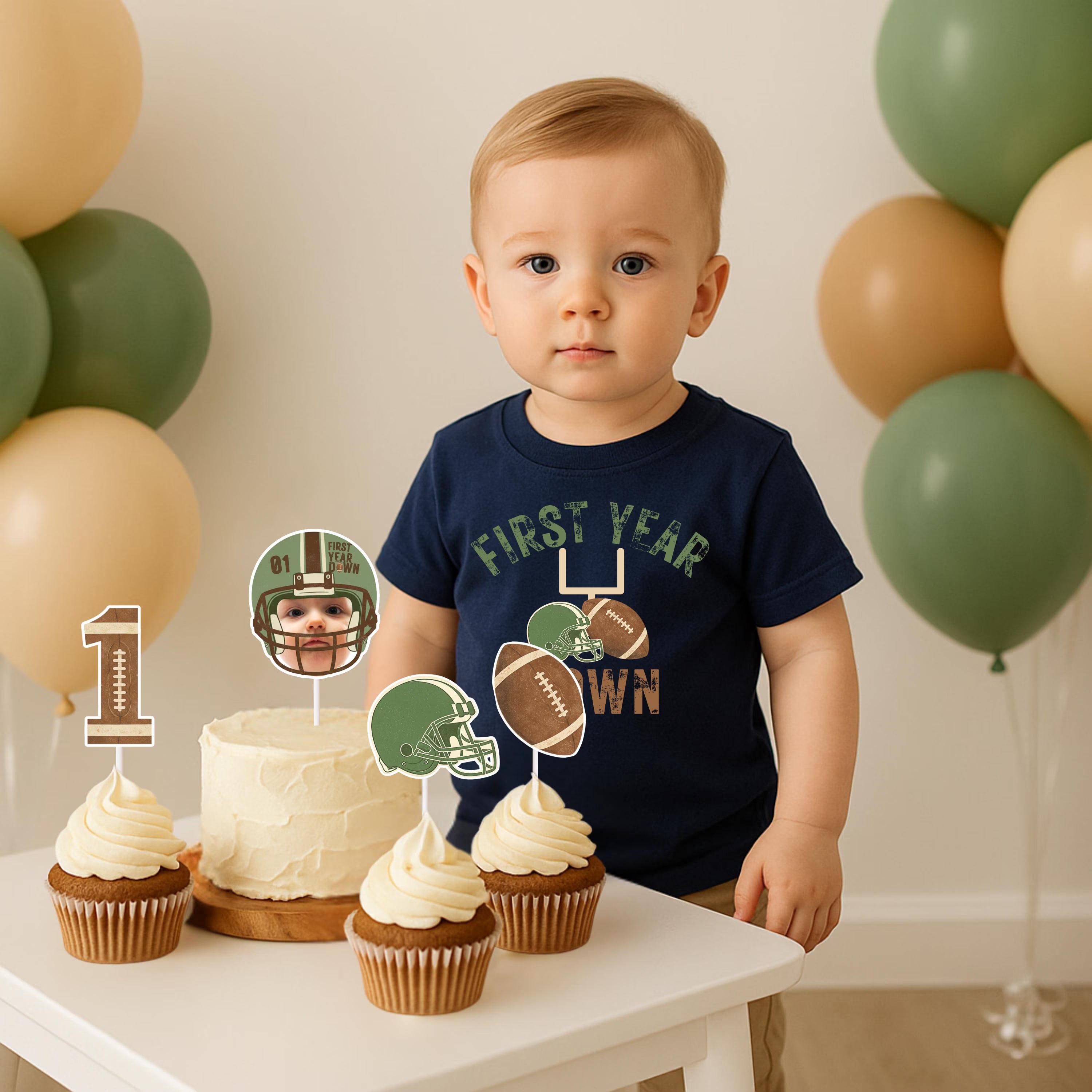 A young boy standing by a smash cake decorated with custom football helmet and '1' yard line cupcake toppers for a Rookie of the Year theme.