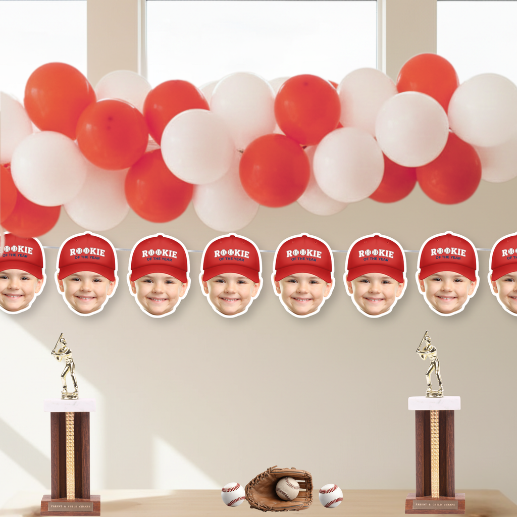 Rookie of the Year photo baseball banner featuring red cap style under red and white balloon garland, personalized face cutouts for baseball birthday party decorations and dessert table backdrop.