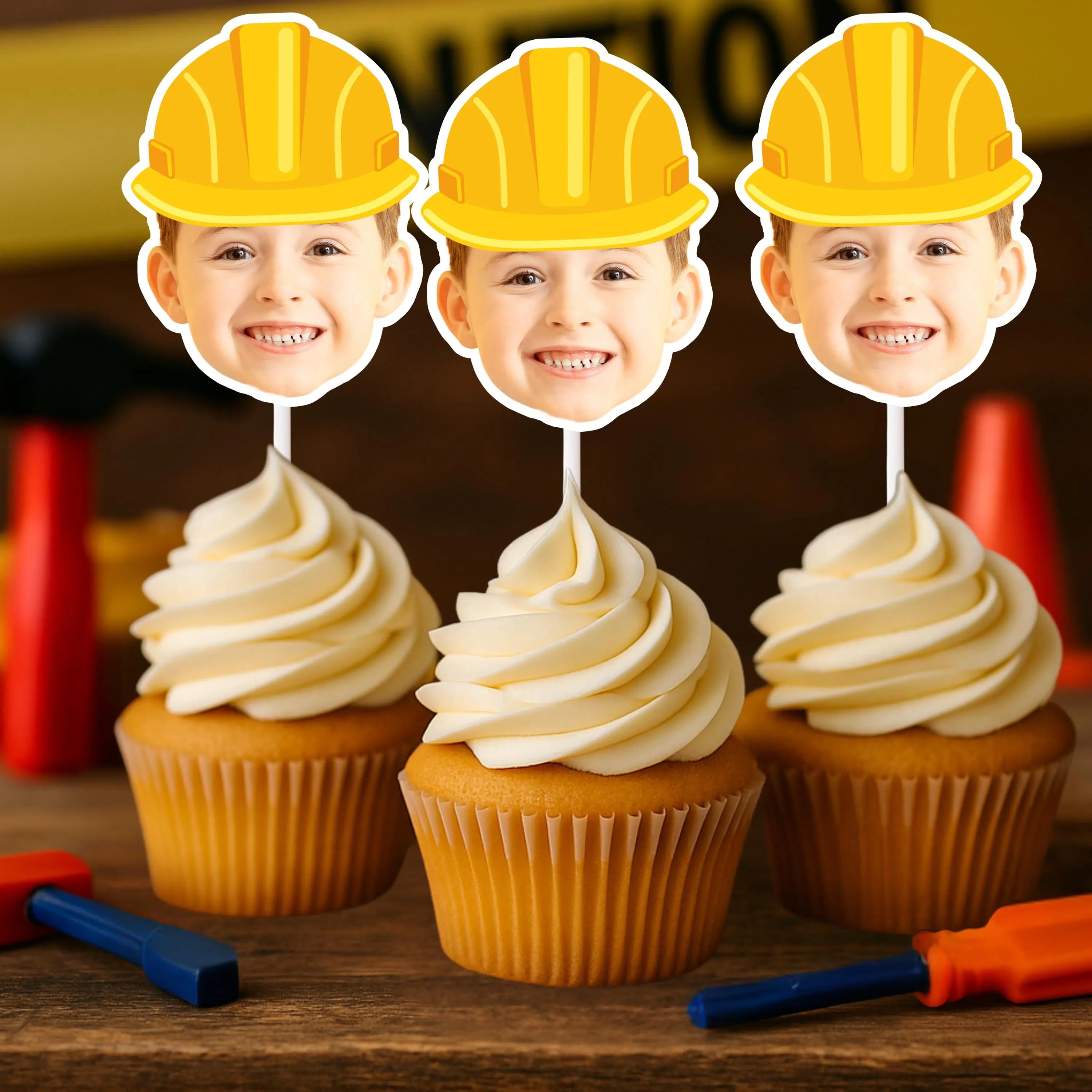 Three cupcakes with yellow construction hats on toppers, surrounded by construction-themed items.